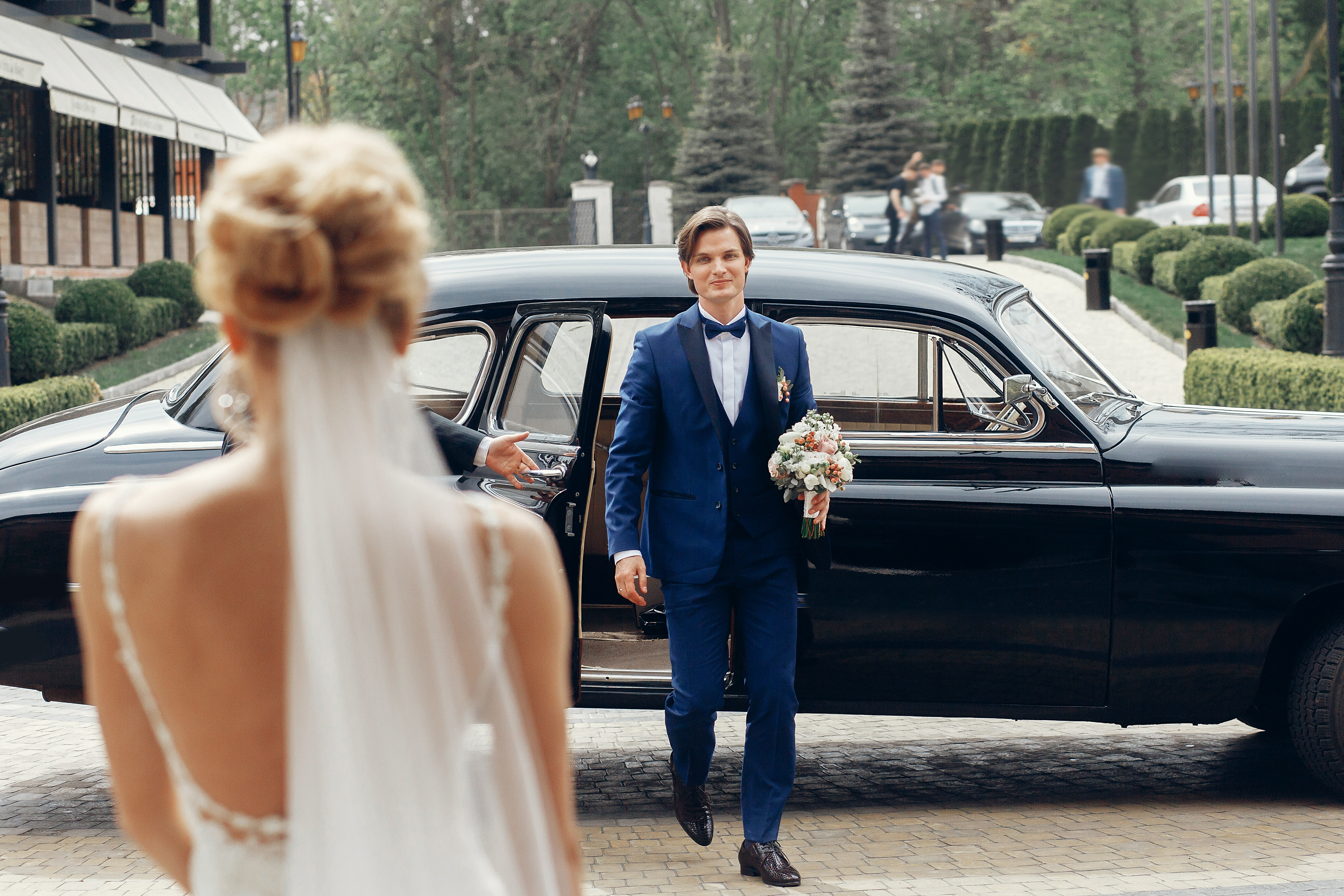 Handsome happy groom with wedding bouquet walking out of black r
